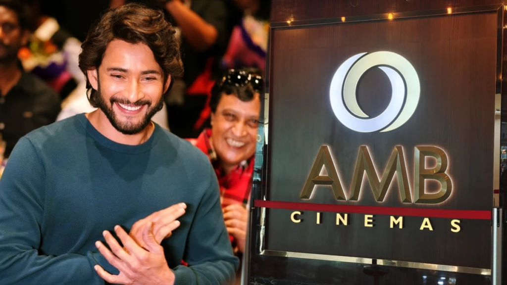 A smiling man in a teal sweater stands beside an illuminated AMB Cinemas sign.