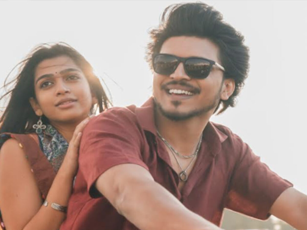 A smiling man in sunglasses and a woman sit close together outdoors.