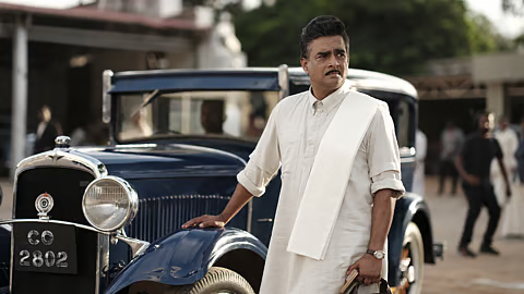 Man in white clothing standing beside a vintage car.
