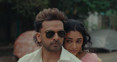 A man in sunglasses with a woman leaning over his shoulder outdoors